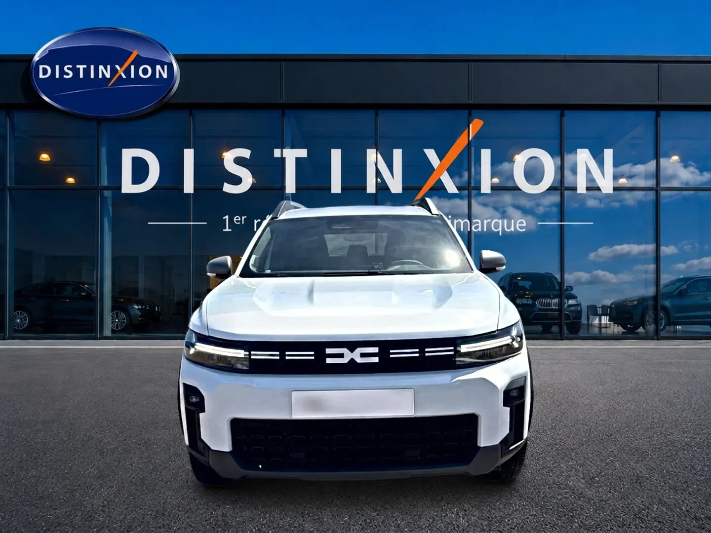 Vue avant d'un Dacia Bigster blanc 2026 avec calandre noire et logo distinctif, devant une vitrine de concession.