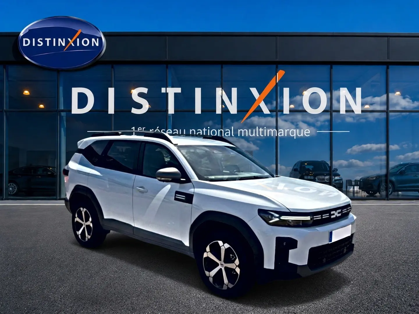 Dacia Bigster blanc vue 3/4 avant droit, avec barres de toit et jantes alliage devant showroom Distinxion.