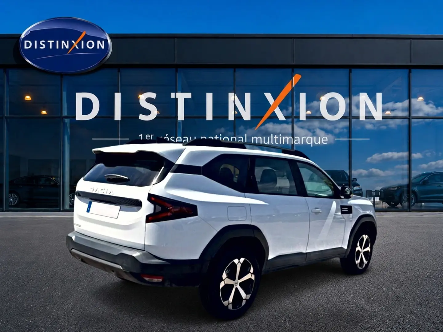 Vue 3/4 arrière droite du SUV blanc Dacia Bigster 2026 avec jantes alu et barres de toit noires.