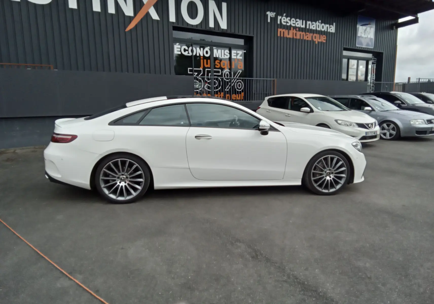 Profil côté gauche d'une Mercedes Classe E Coupé blanche AMG Line 220D 2020 avec jantes alliage et toit panoramique.