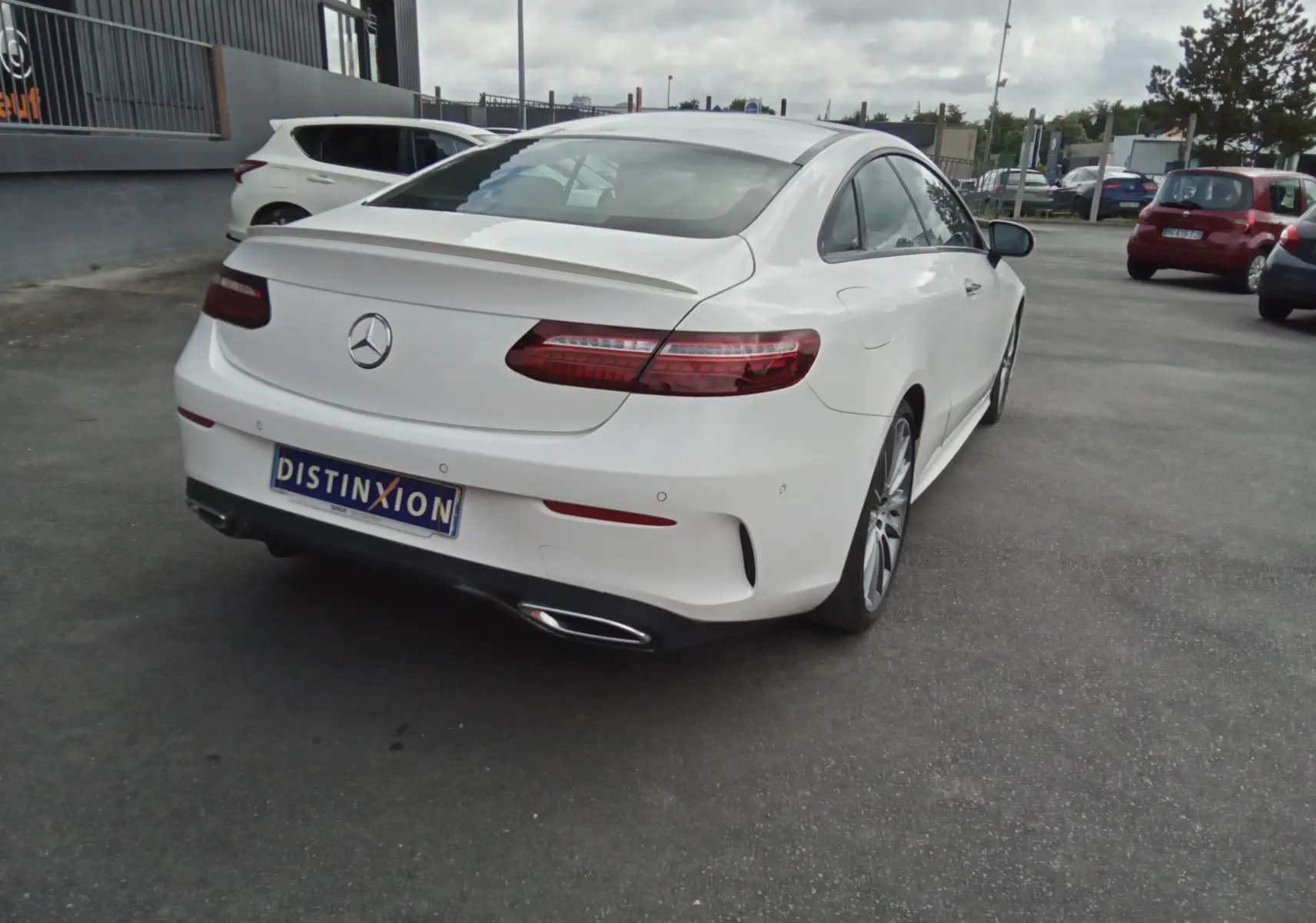 Vue 3/4 arrière droite d'une Mercedes Classe E Coupé 220D AMG Line blanche avec feux arrière LED et double sortie d'échappement chromée.