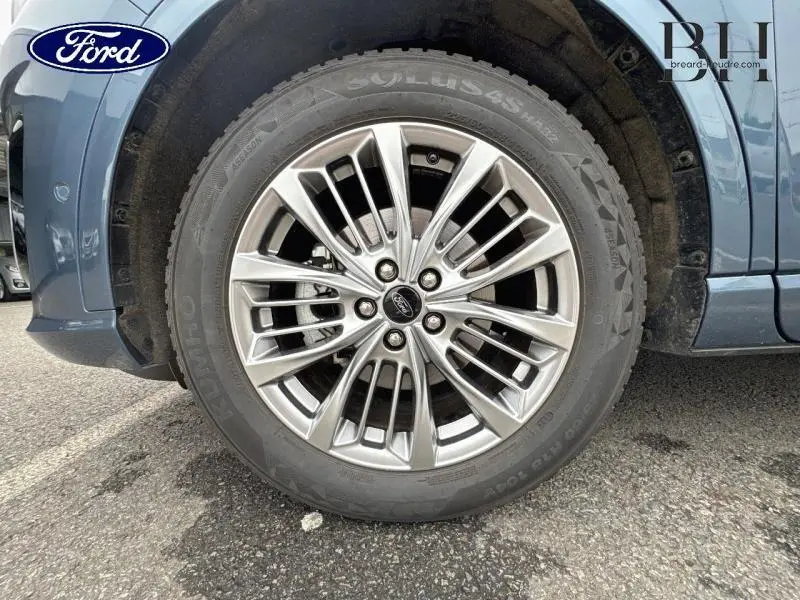 Gros plan sur la roue avant droite en jante alu du Ford Kuga bleu azur métallisé 2022 avec logo Ford central.