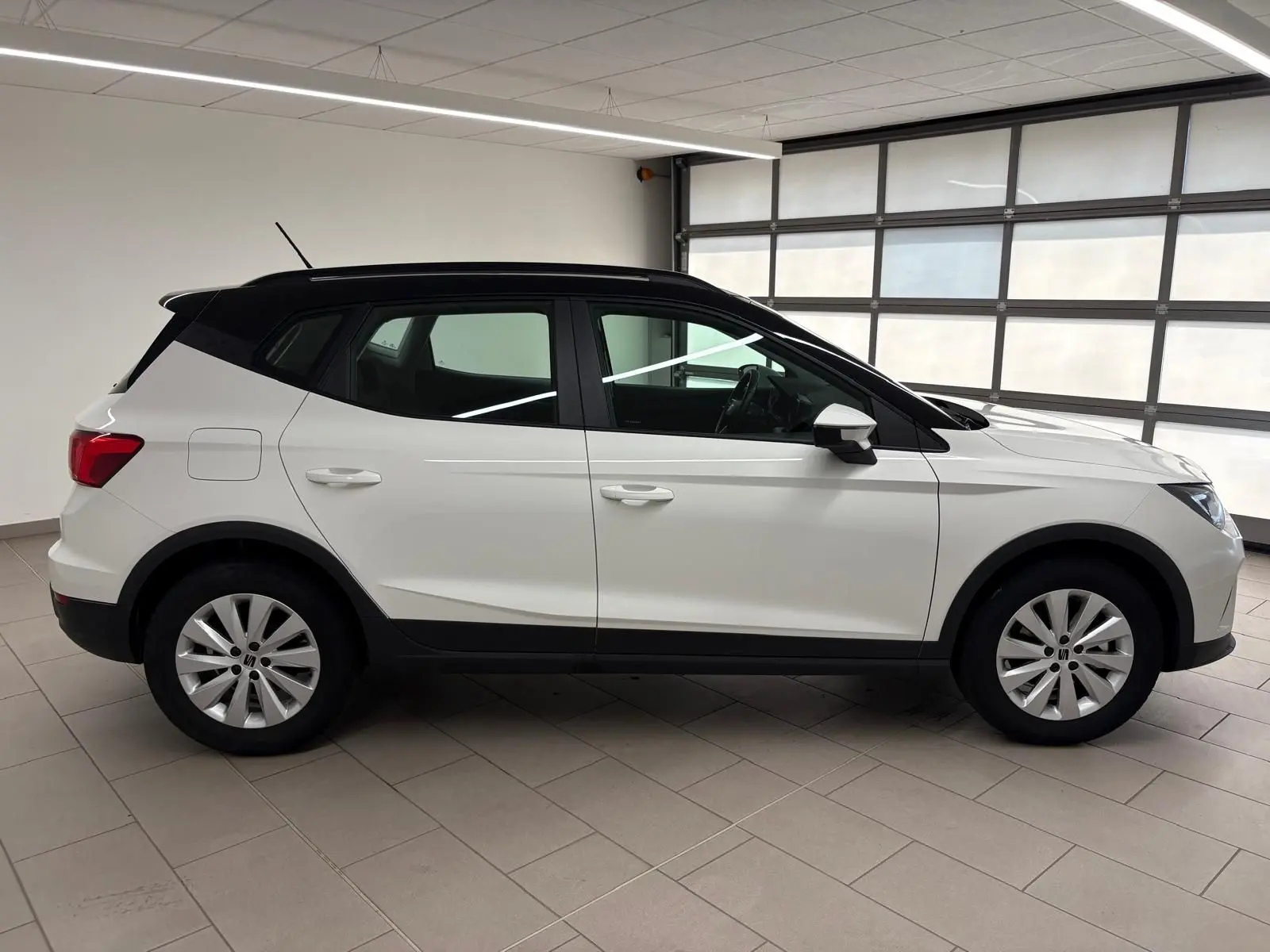 Vue de profil côté gauche du SEAT Arona 2023 blanc avec toit noir, soulignant sa silhouette compacte et ses jantes argentées.
