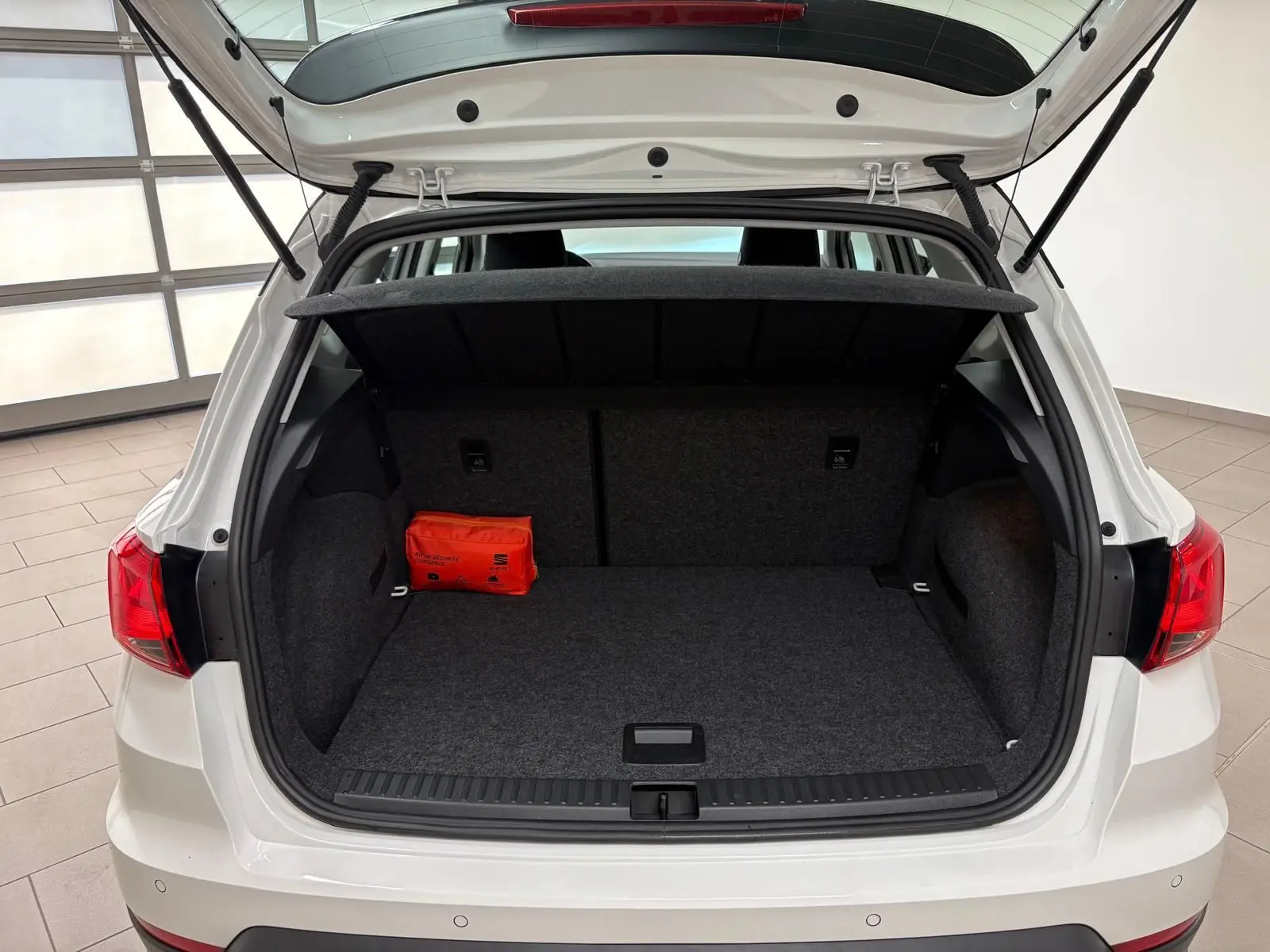 Coffre ouvert vue arrière d'une SEAT Arona blanc toit noir, avec tapis gris et trousse de secours orange à gauche.