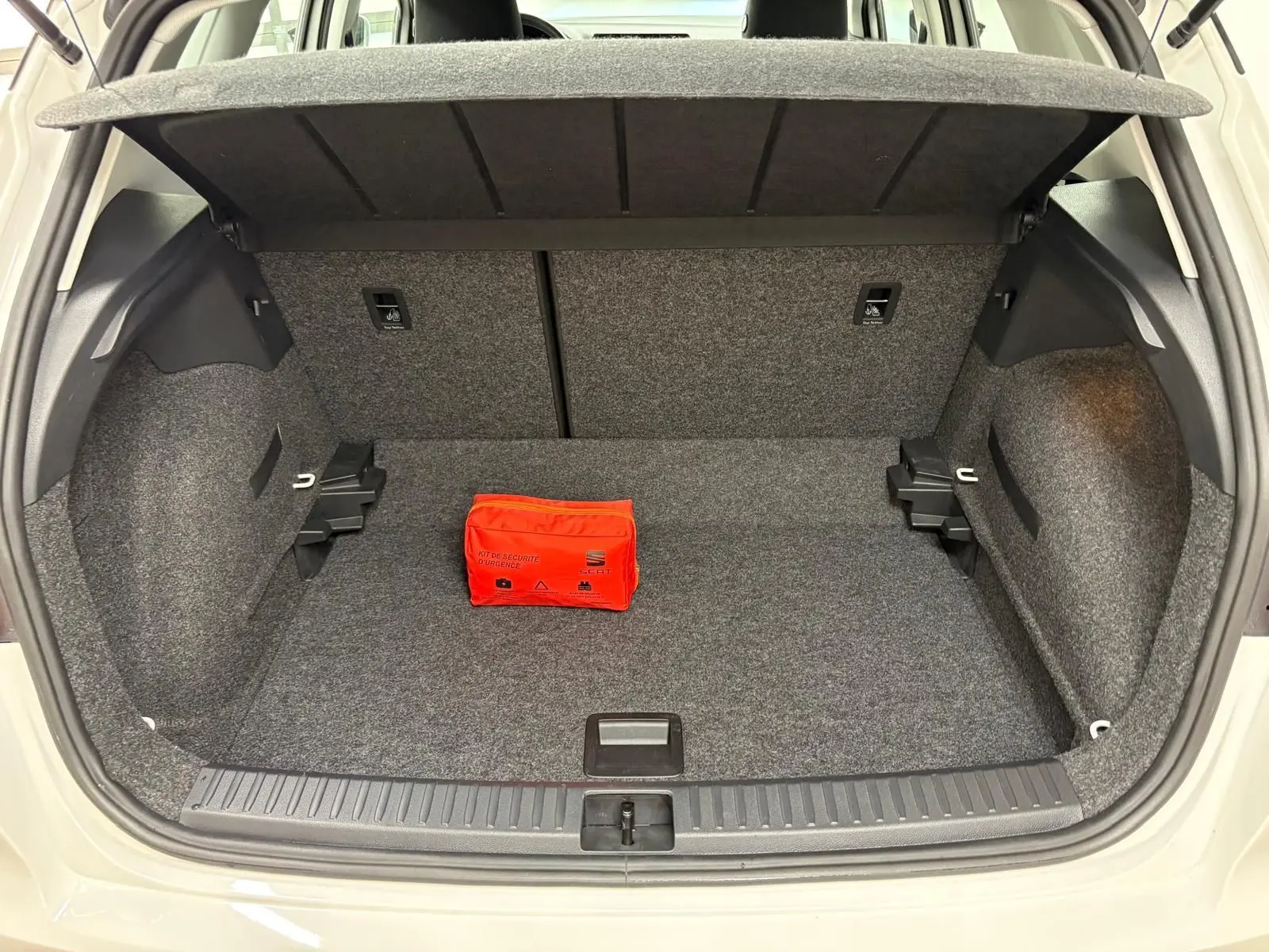 Coffre ouvert d'un SEAT Arona blanc toit noir, vue arrière, avec kit de sécurité rouge posé à l'intérieur.