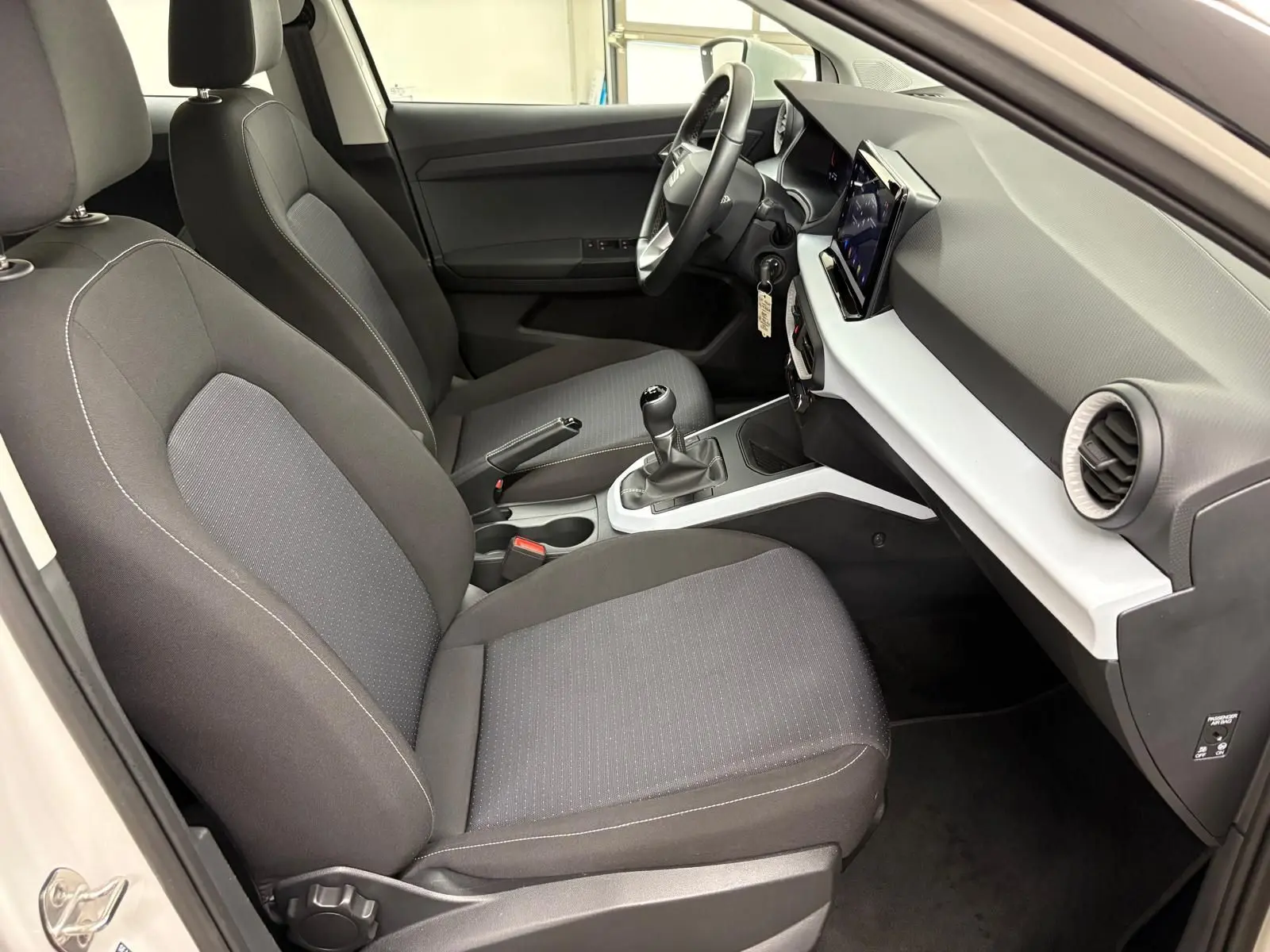 Intérieur avant droit du SEAT Arona 2023 avec sièges gris, tableau de bord blanc et noir, et boîte manuelle visible.