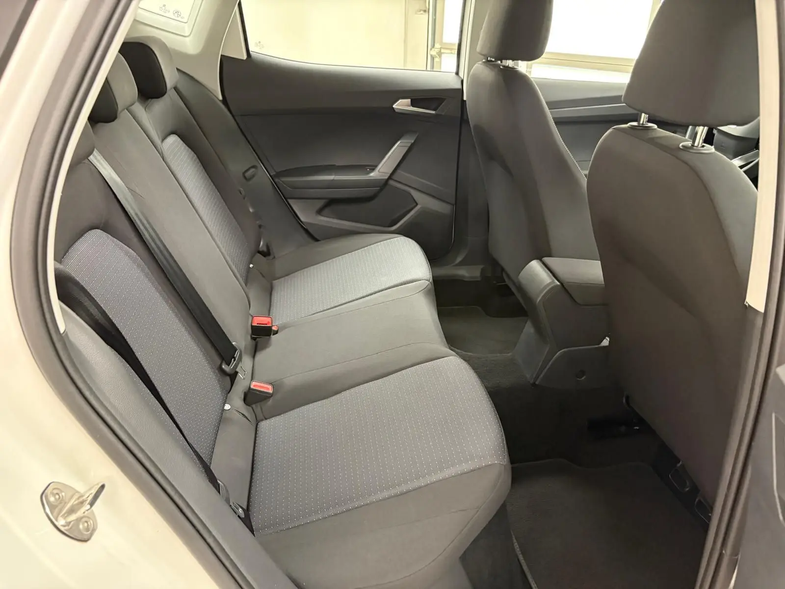 Vue intérieure côté gauche des sièges arrière gris foncé du SEAT Arona 2023 avec porte ouverte et accoudoir central avant visible.