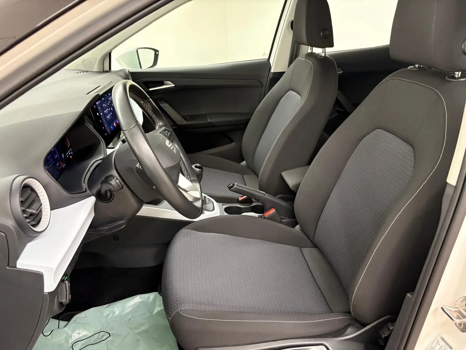 Intérieur avant du SEAT Arona 2023, sièges noirs avec coutures blanches, volant multifonction et tableau de bord moderne.
