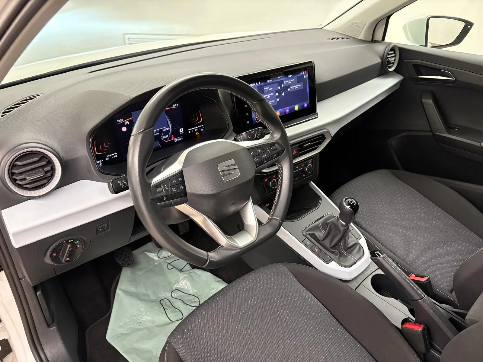 Intérieur du SEAT Arona 2023 vu côté conducteur, tableau de bord noir et gris avec volant multifonction et boîte manuelle.