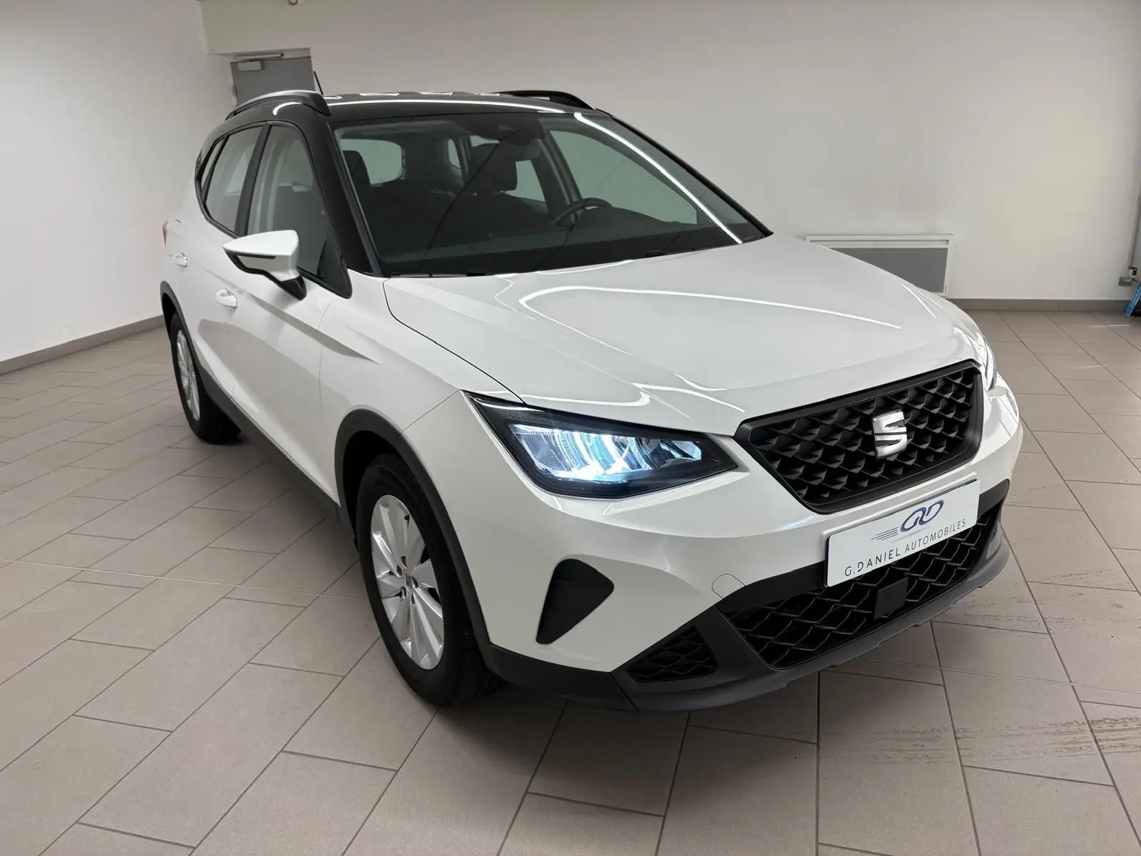 SEAT Arona blanc avec toit noir en 3/4 avant droit, phares allumés et calandre noire distinctive.