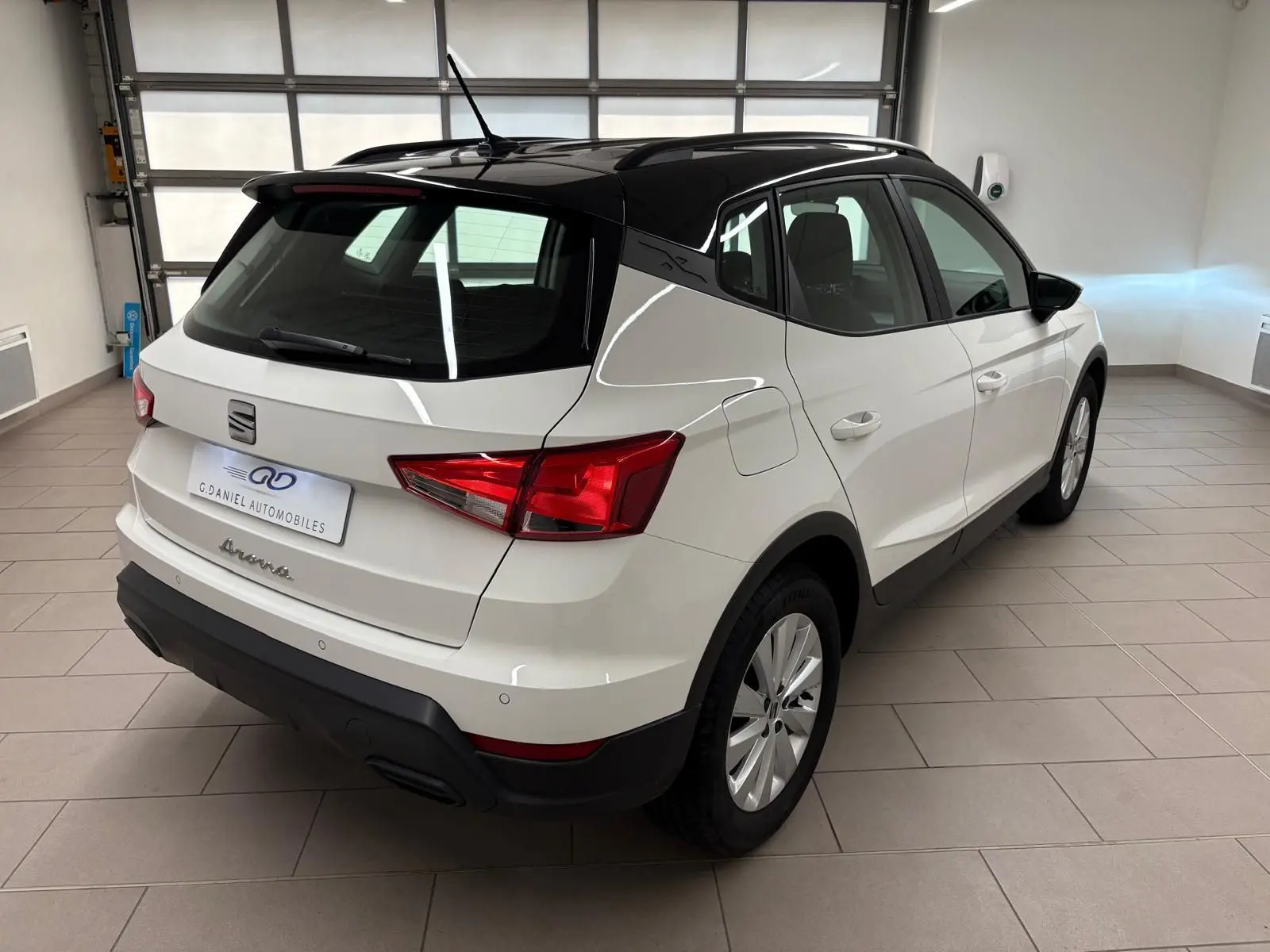 Vue 3/4 arrière droite du SEAT Arona blanc avec toit noir, soulignant son design compact et élégant en intérieur showroom.