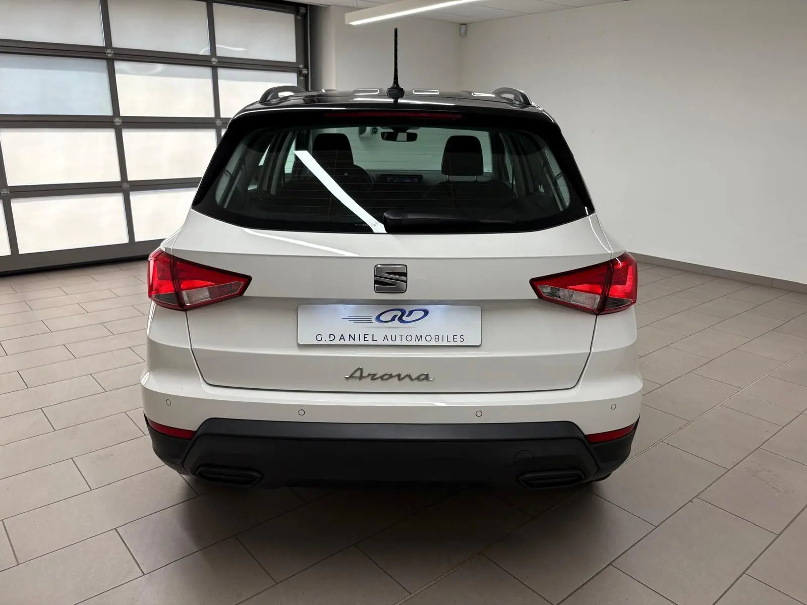 Vue arrière d'un SEAT Arona blanc avec toit noir, dans un showroom lumineux, soulignant ses feux arrière rouges.