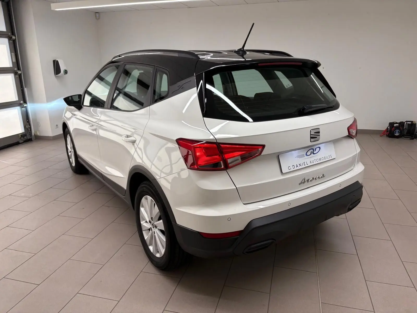 Vue 3/4 arrière droite d'un SEAT Arona blanc avec toit noir, stationné en intérieur sur carrelage gris.