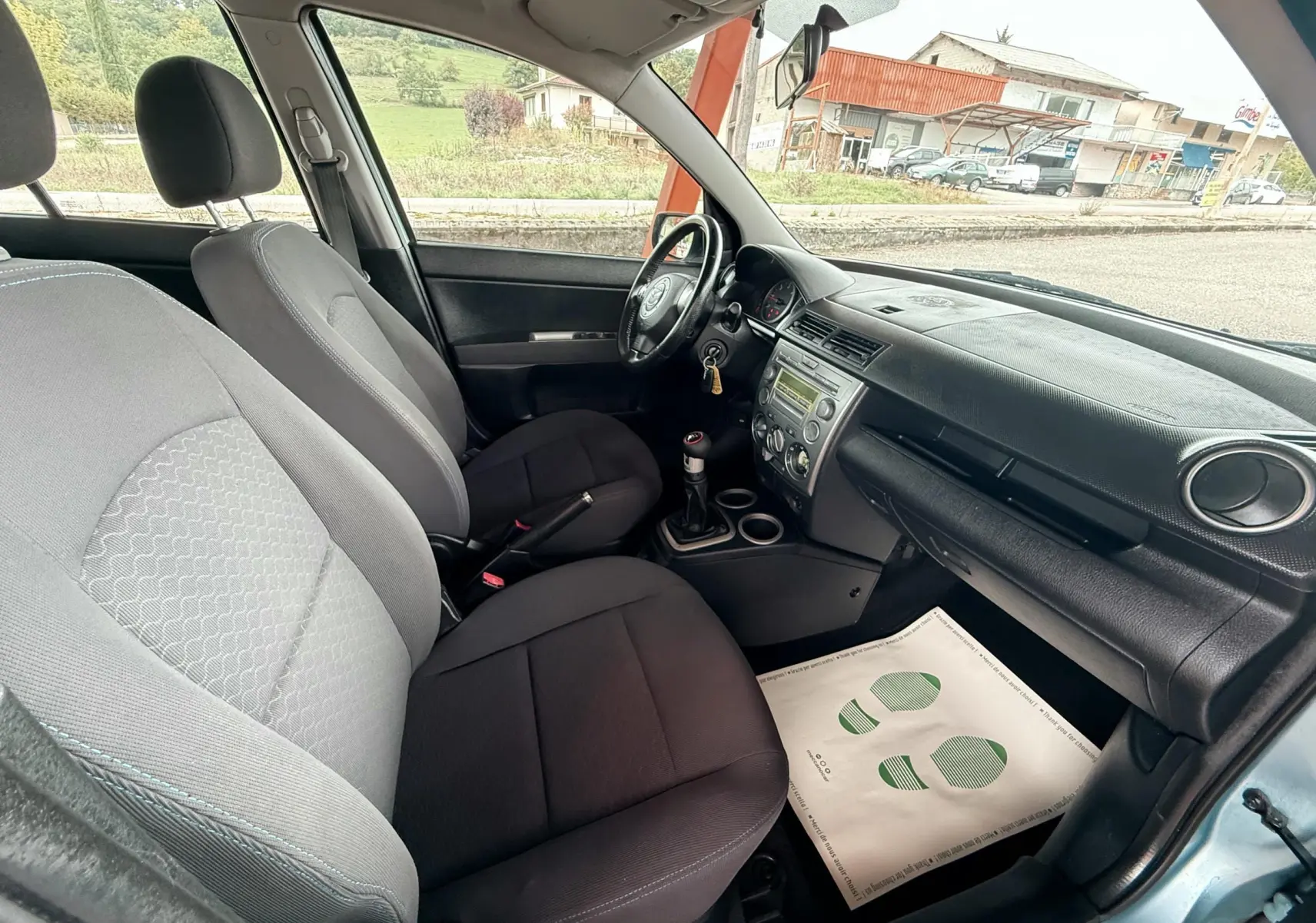 Intérieur noir et gris de la Mazda2 2004, vue côté conducteur montrant sièges, volant et tableau de bord.