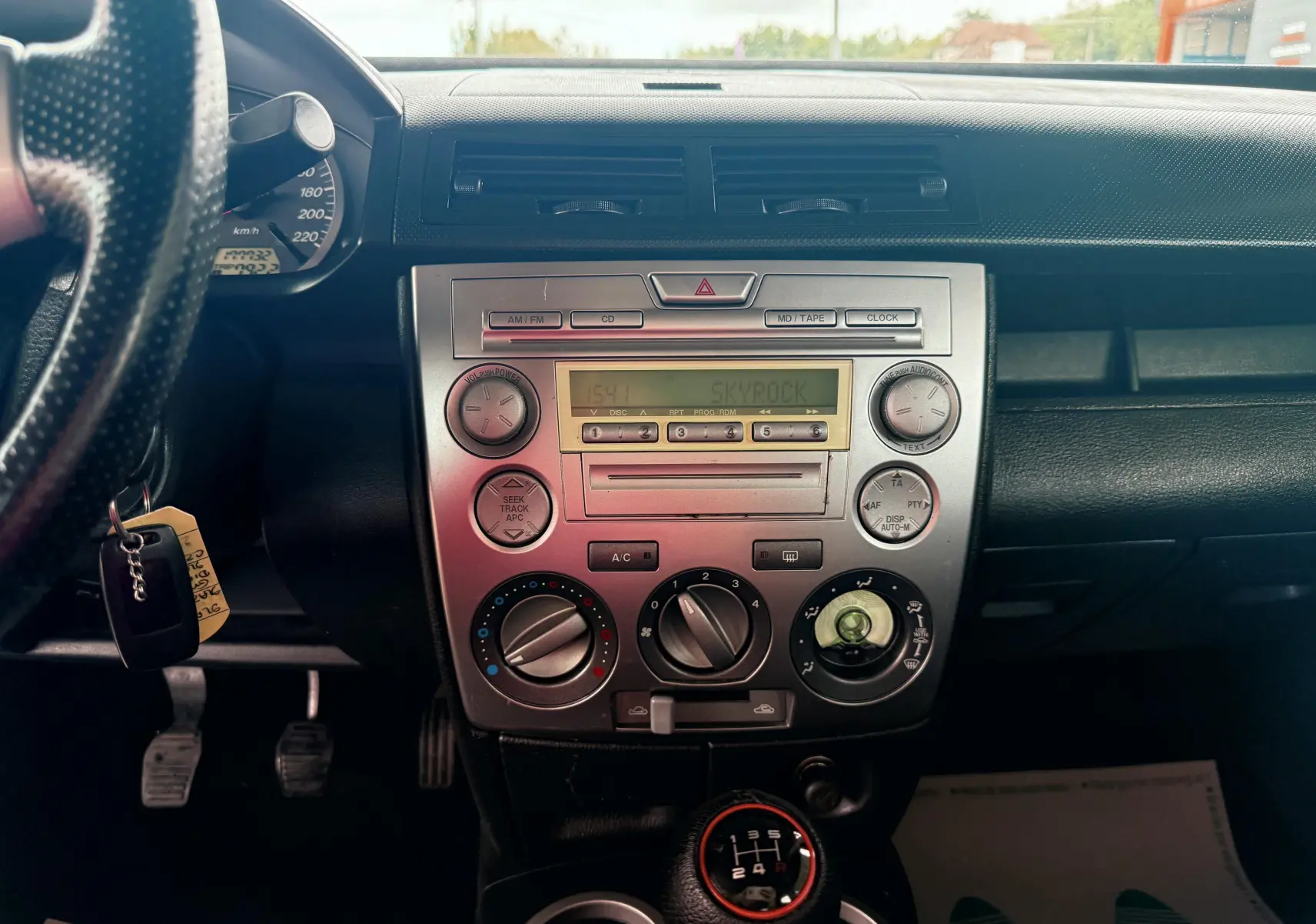 Tableau de bord et console centrale d'une Mazda2 gris 2004, vue frontale avec radio et commande manuelle de climatisation.