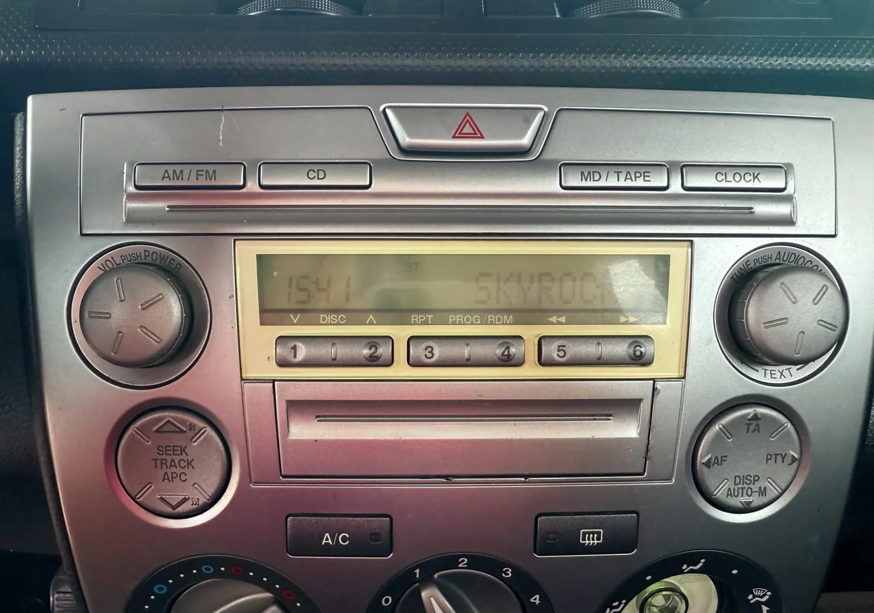 Console centrale de la Mazda2 grise 2004 montrant la radio CD et les commandes de climatisation en gros plan.