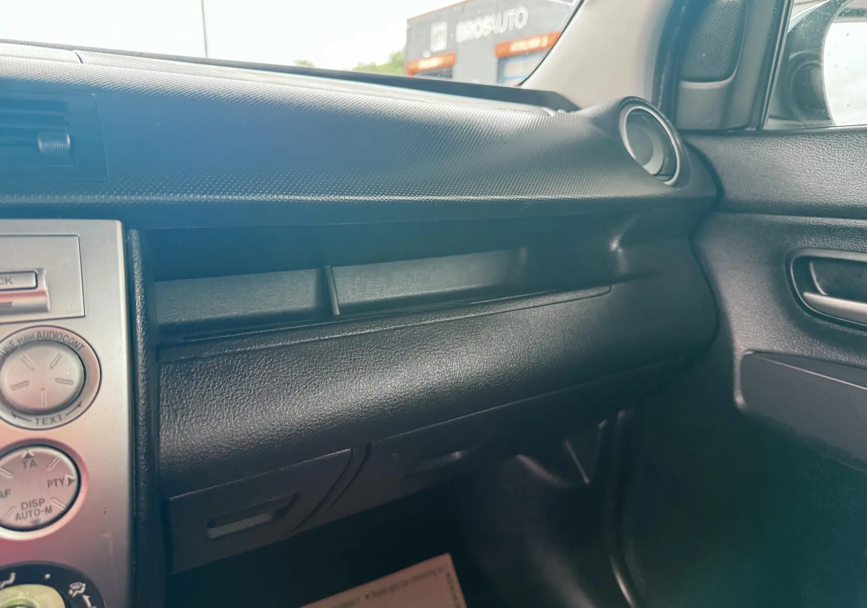 Vue intérieure côté passager du tableau de bord noir de la Mazda2 gris 2004 avec détails de la console centrale et portière.