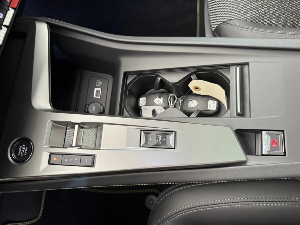 Vue plongeante sur la console centrale grise du Peugeot 308 Hybrid 136 e-DCS6 GT avec boutons de boîte auto et clés dans porte-gobelets.