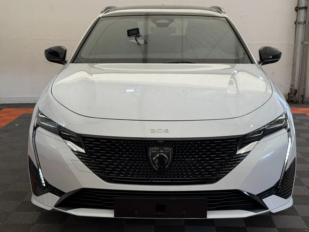 Vue frontale d'une Peugeot 308 Hybrid 136 e-DCS6 GT blanche avec calandre noire et feux LED distinctifs.
