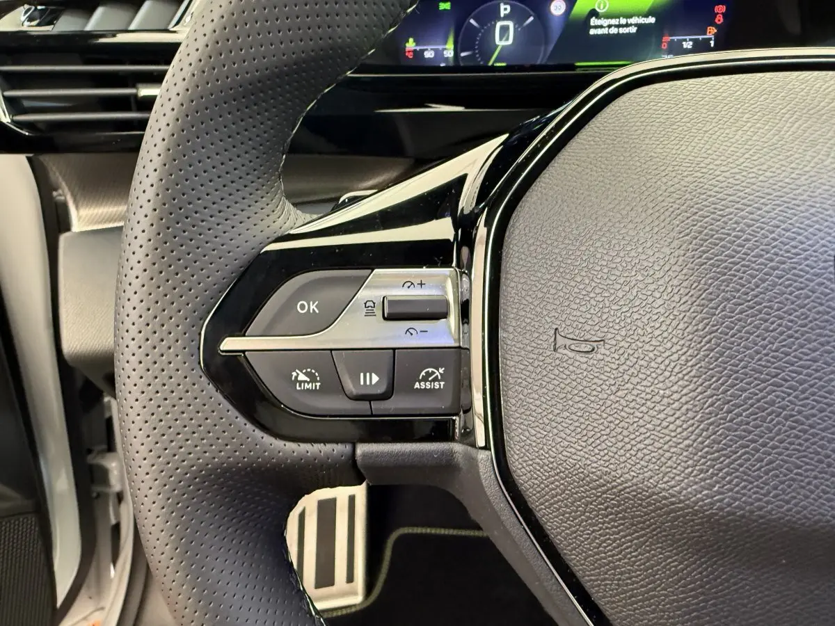 Gros plan sur le volant cuir perforé gauche du Peugeot 308 Hybrid 2024 avec commandes intégrées et tableau de bord digital.