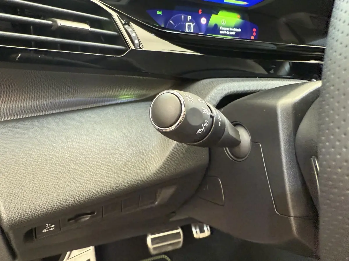 Gros plan sur la commande d'éclairage à gauche du volant dans l'habitacle noir du Peugeot 308 Hybrid 2024.