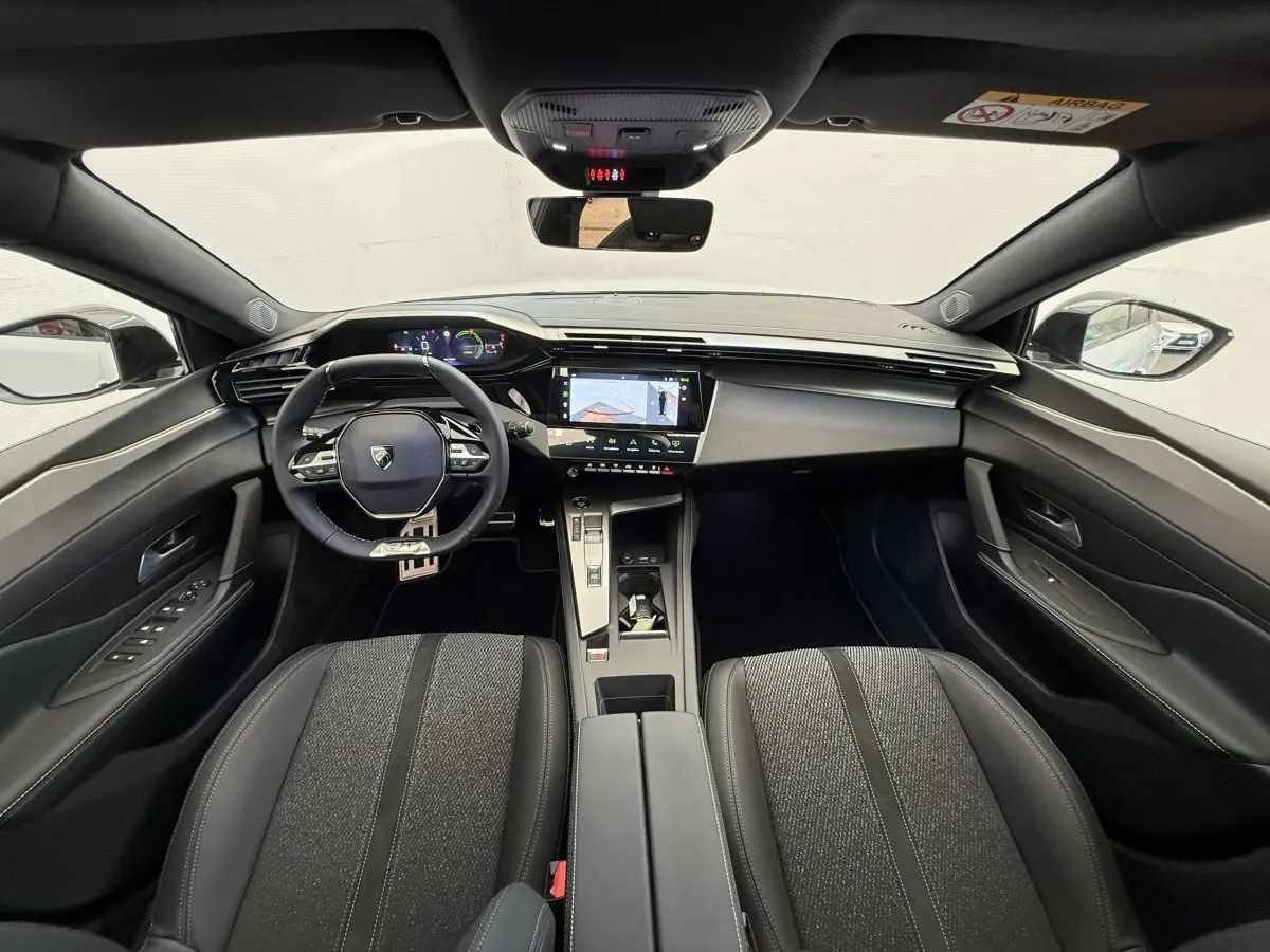 Vue intérieure avant du Peugeot 308 Hybrid 136 e-DCS6 GT 2024, tableau de bord moderne avec écran tactile central et volant cuir.