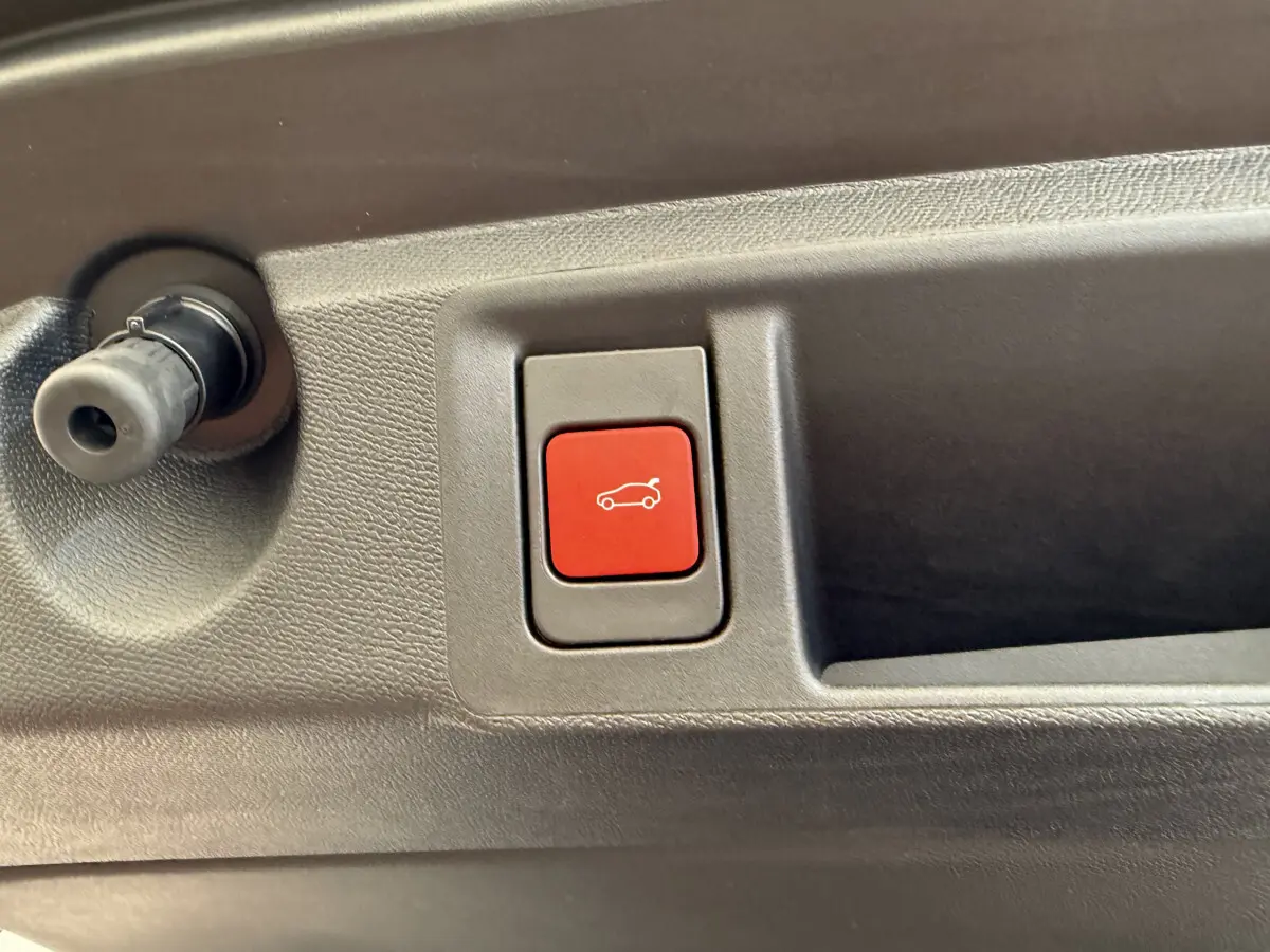 Gros plan sur le bouton rouge d'ouverture électrique du coffre dans l'habitacle d'une Peugeot 308 Hybrid blanche.