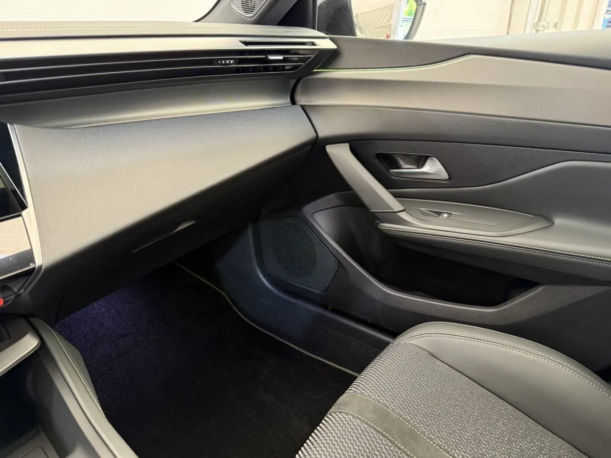 Vue intérieure côté passager de la Peugeot 308 Hybrid 136 e-DCS6 GT 2024 avec sellerie grise et tableau de bord noir.