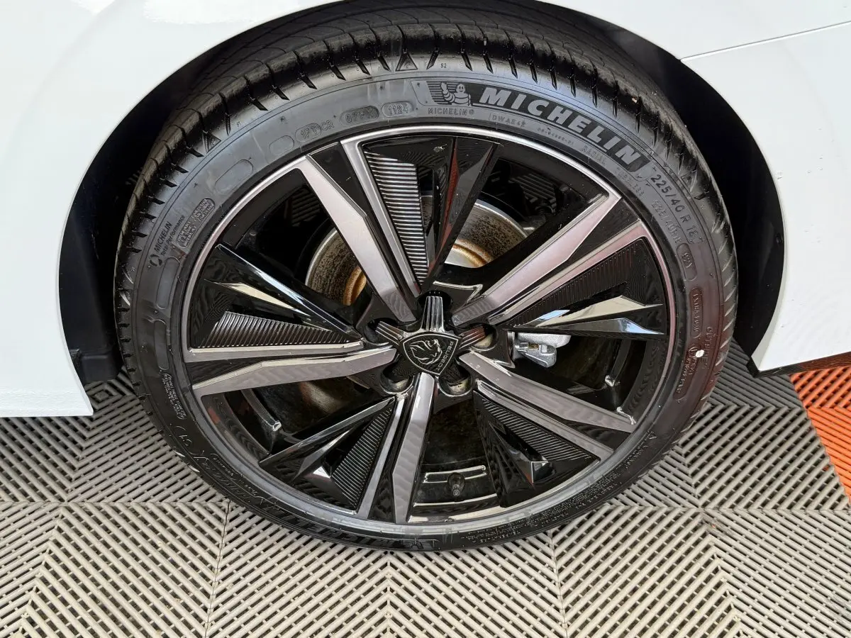 Gros plan sur la roue avant droite blanche d'une Peugeot 308 Hybrid 136 e-DCS6 GT avec jante noire et argentée distinctive.
