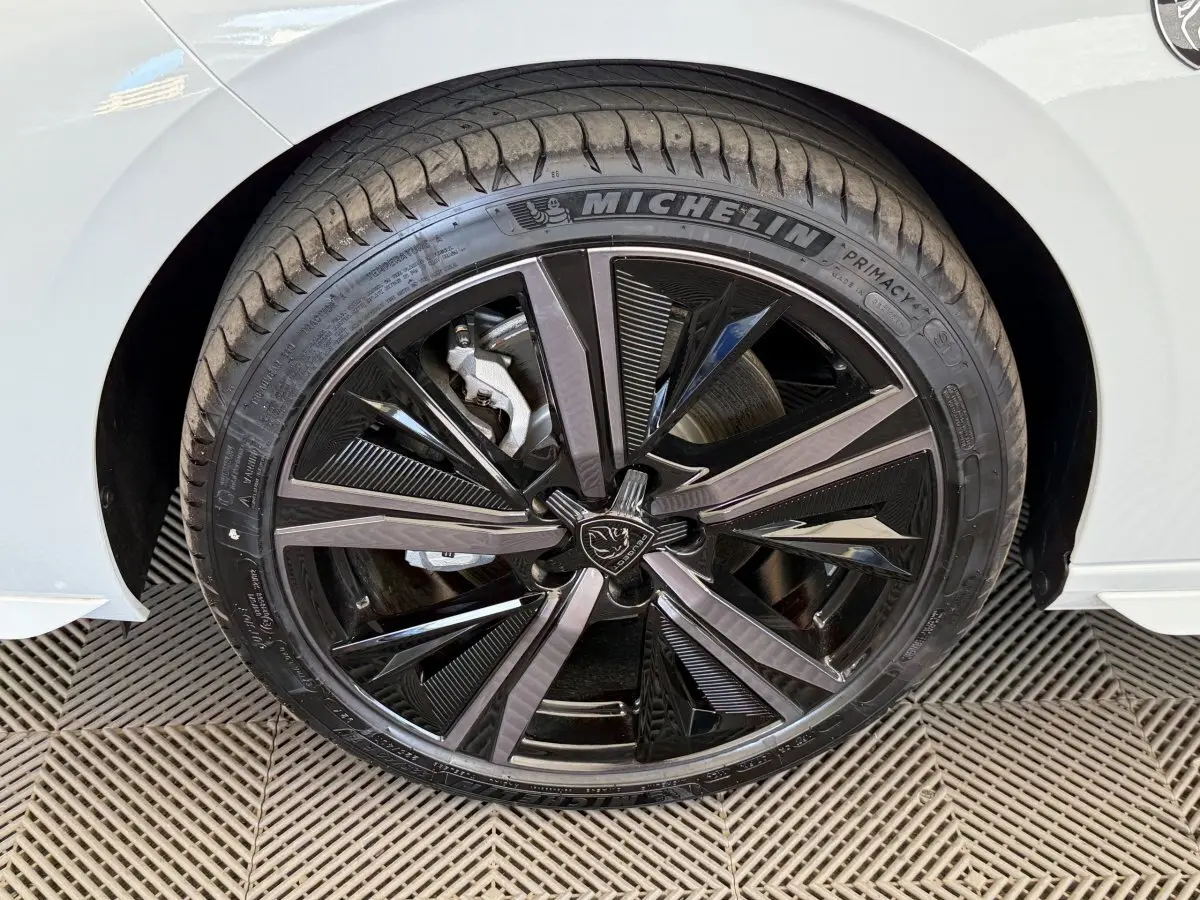 Gros plan sur la roue avant droite de la Peugeot 308 Hybrid 136 e-DCS6 GT blanche avec jante noire brillante et logo lion central.