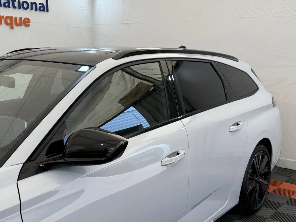 Vue latérale droite d'une Peugeot 308 Hybrid 136 e-DCS6 GT blanche avec toit noir et rétroviseur noir brillant.