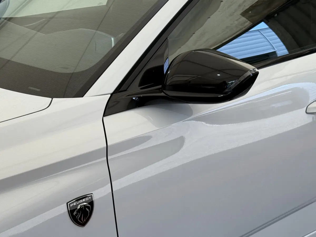 Détail du côté gauche blanc d'une Peugeot 308 Hybrid 136 e-DCS6 GT avec rétroviseur noir brillant et logo lion.