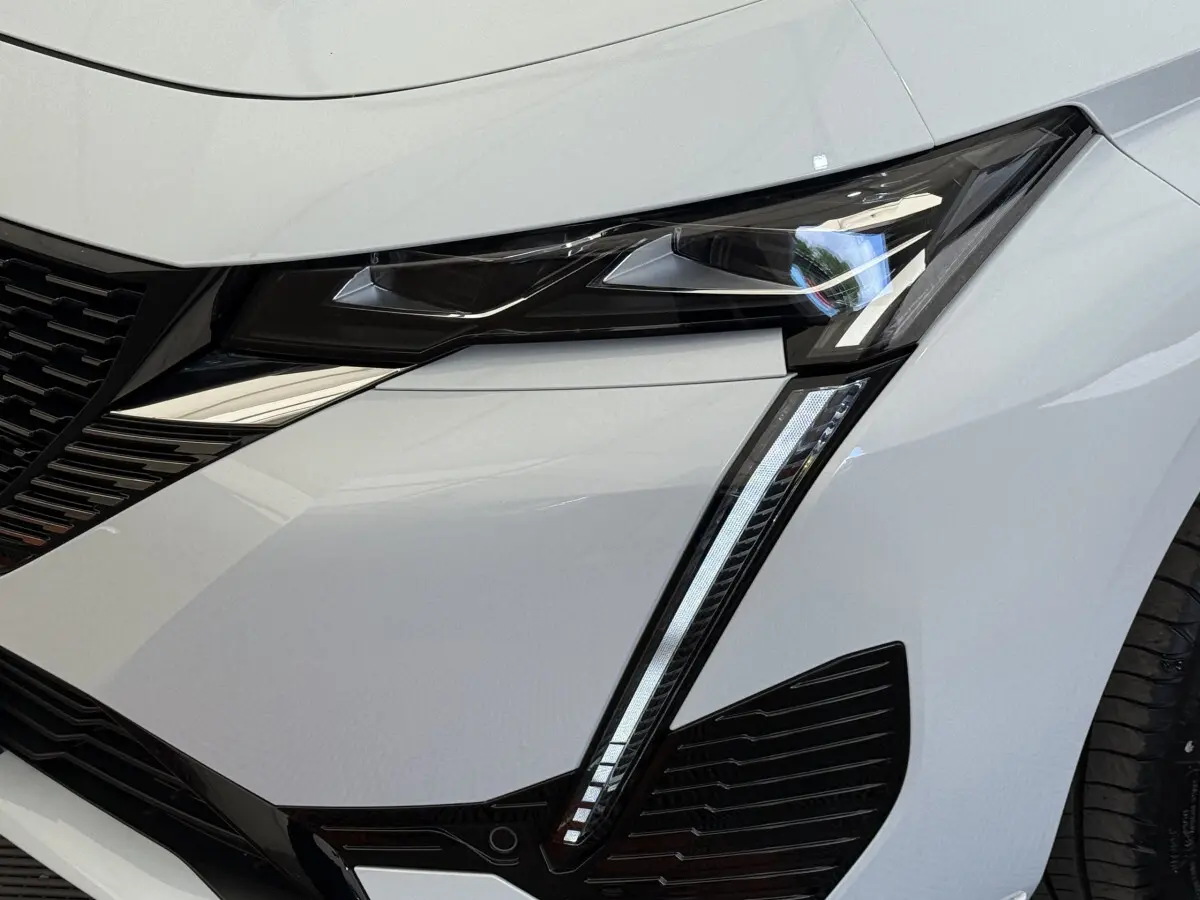 Gros plan sur le phare avant droit blanc de la Peugeot 308 Hybrid 136 e-DCS6 GT avec signature lumineuse LED distinctive.