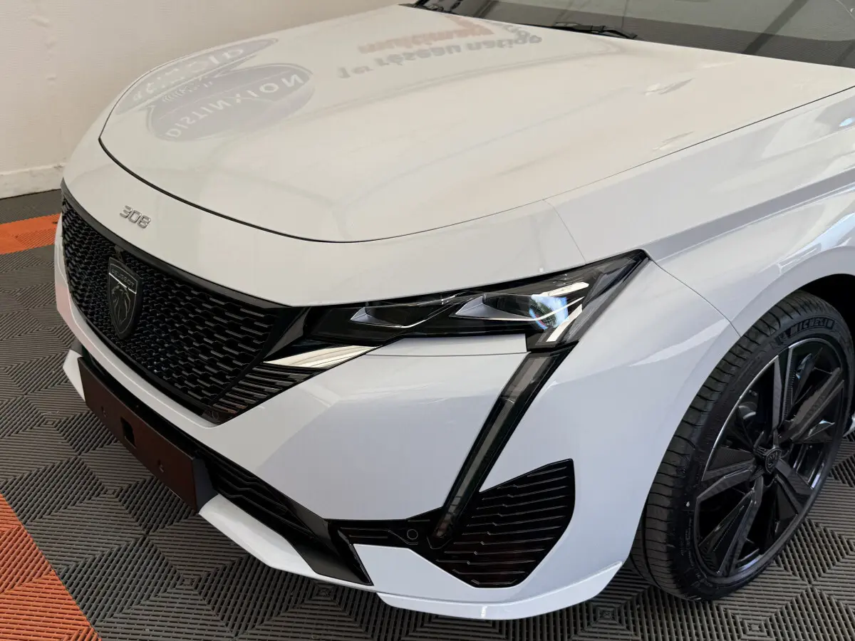 Vue 3/4 avant droit d'une Peugeot 308 Hybrid 136 e-DCS6 GT blanche avec calandre noire et phares LED distinctifs.