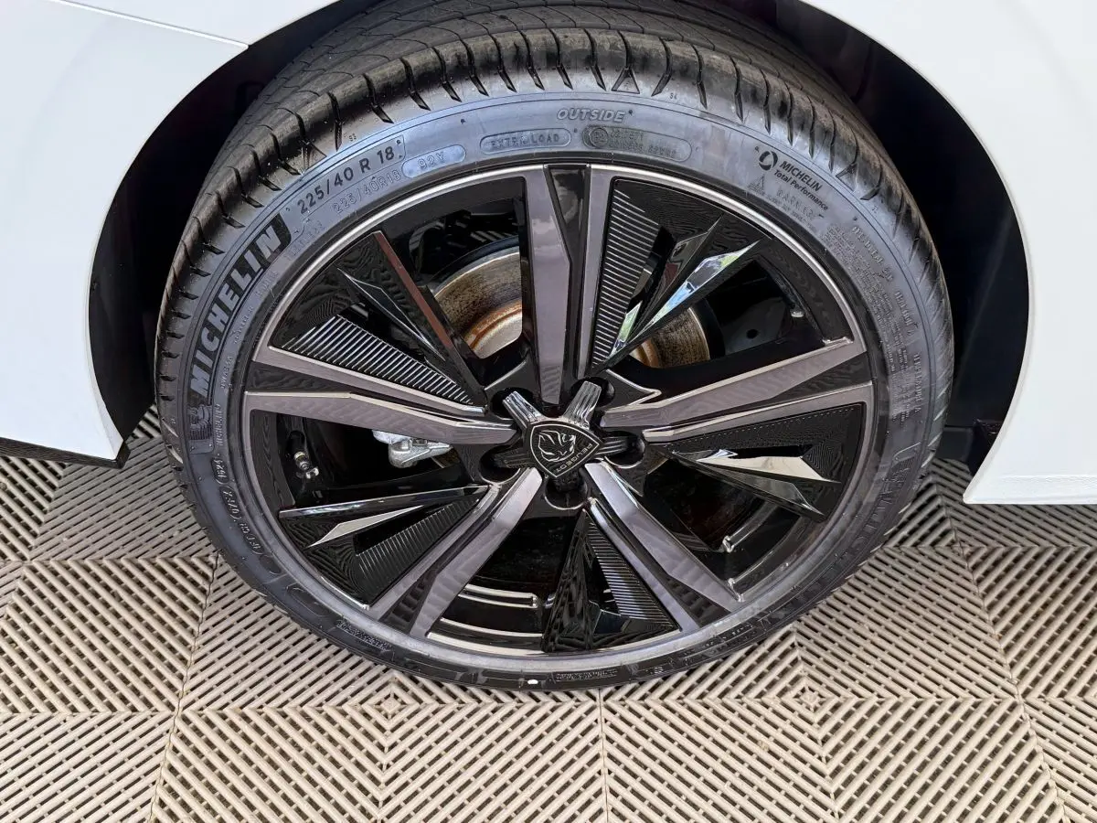 Gros plan sur la roue avant droite noire brillante de la Peugeot 308 Hybrid 136 e-DCS6 GT blanche, pneu Michelin visible.