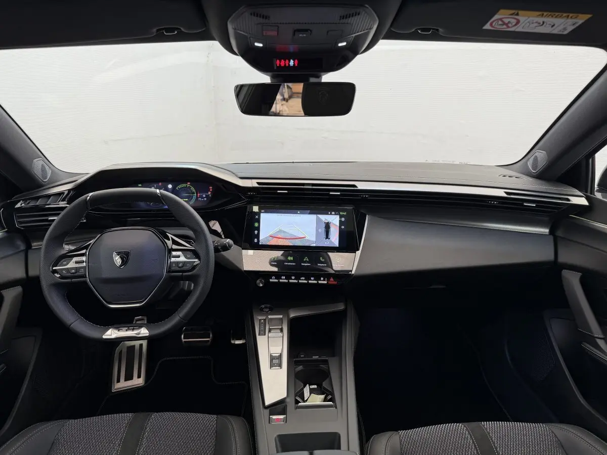 Intérieur noir de la Peugeot 308 Hybrid 136 e-DCS6 GT 2024, vue frontale sur tableau de bord et volant multifonctions.
