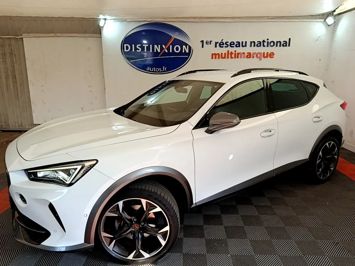 Vue 3/4 avant droite d'un CUPRA Formentor blanc avec jantes noires et détails gris métallisé en intérieur showroom.
