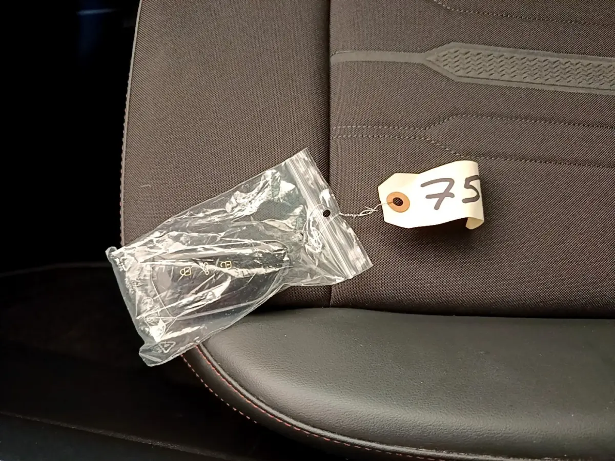 Gros plan sur la clé de contact dans un sachet plastique posée sur un siège tissu gris foncé avec surpiqûres rouges.