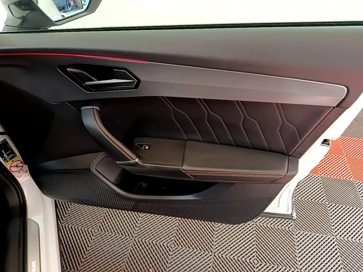 Vue intérieure côté gauche de la porte avant d'une CUPRA Formentor 2023 avec garniture noire et surpiqûres rouges.