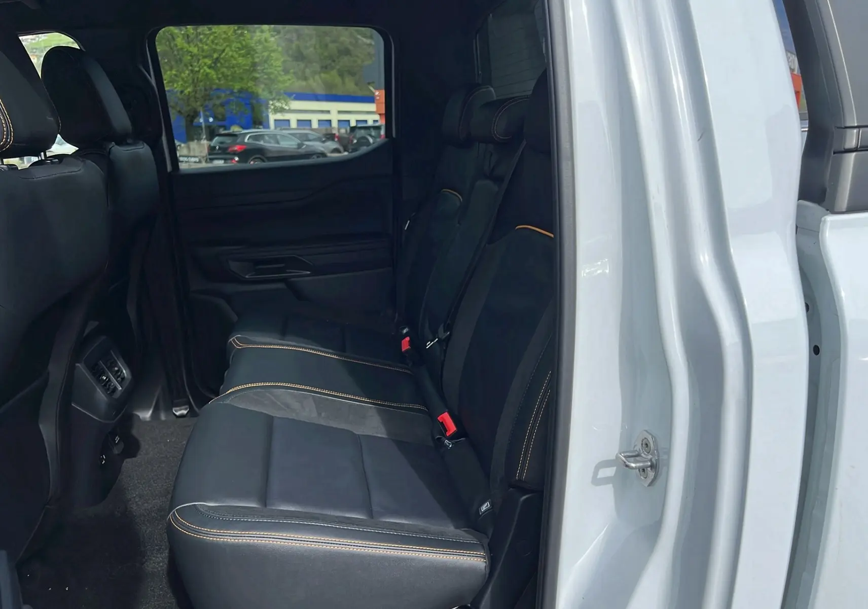 Vue intérieure côté droit sur la banquette arrière en cuir noir avec surpiqûres orange du Ford Ranger blanc glacier 2025.