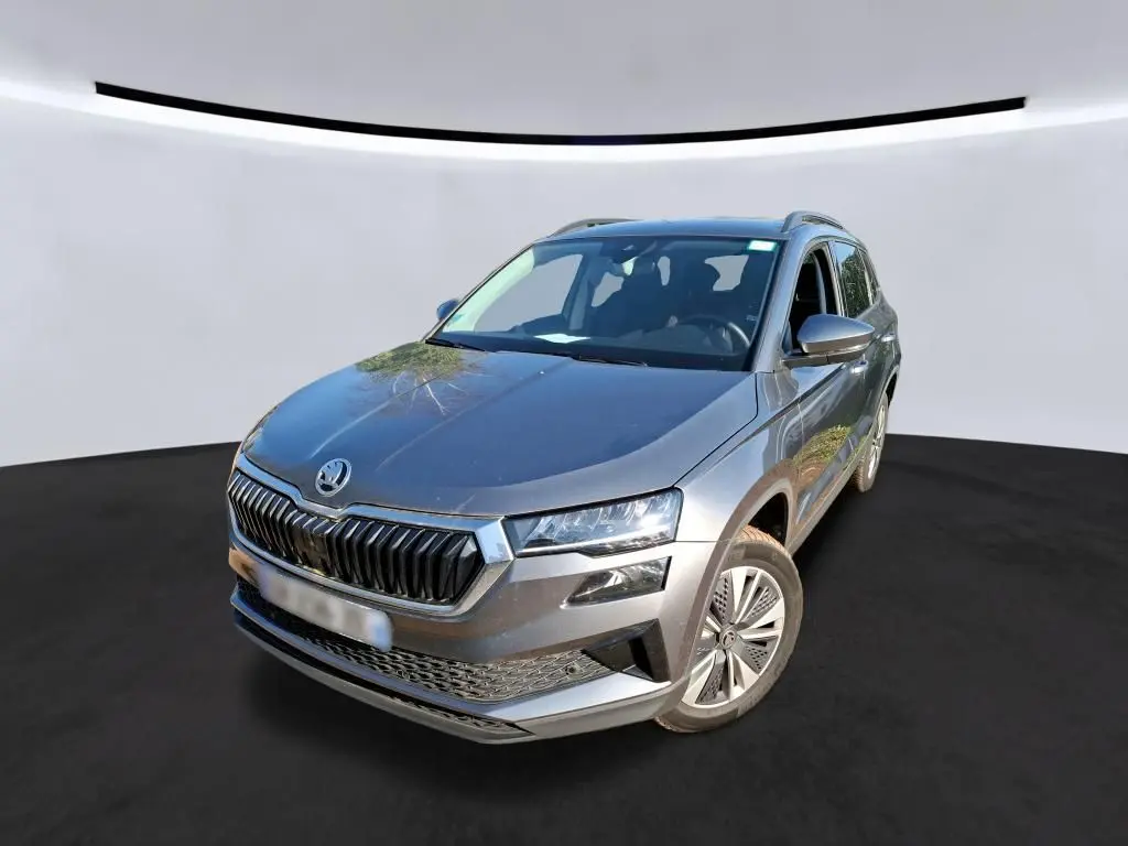 Vue 3/4 avant droite d'un Skoda Karoq gris 2023 avec jantes alu 17'' et calandre chromée, en intérieur showroom.