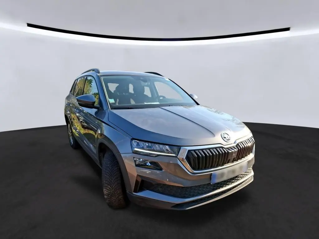 Vue frontale d'un Skoda Karoq gris 2023 avec calandre noire et logo chromé, en intérieur showroom.