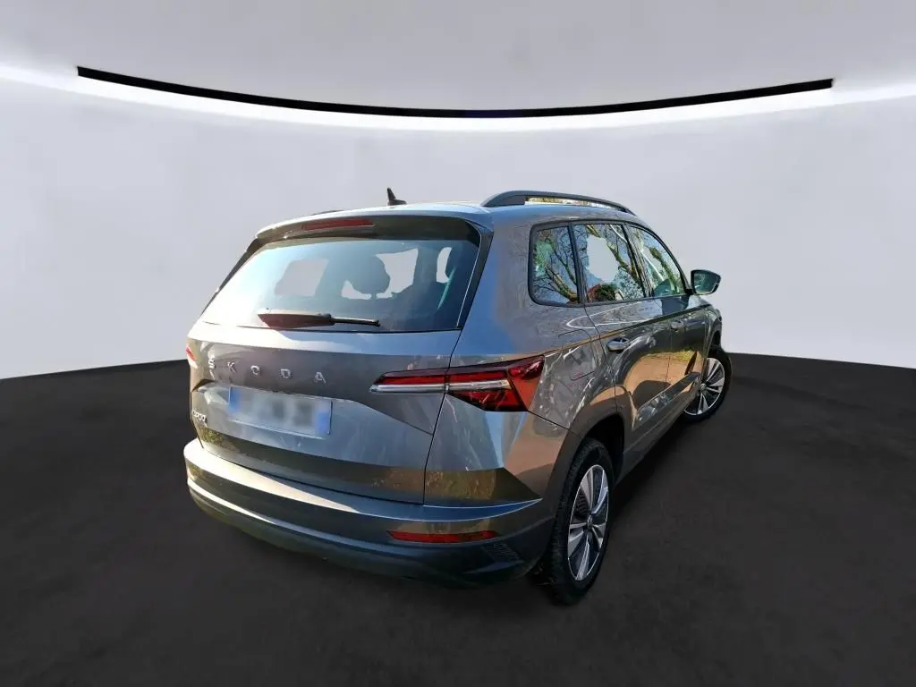 Vue 3/4 avant gauche d’un Skoda Karoq gris métallisé avec calandre chromée et jantes alu 17 pouces en intérieur showroom.