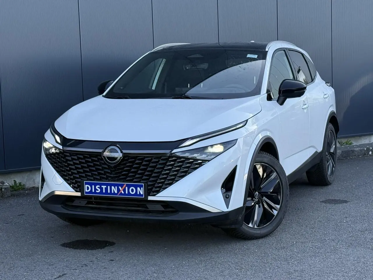 Nissan Qashqai blanc nacré en 3/4 avant droit, avec calandre noire et jantes alliage 19 pouces.