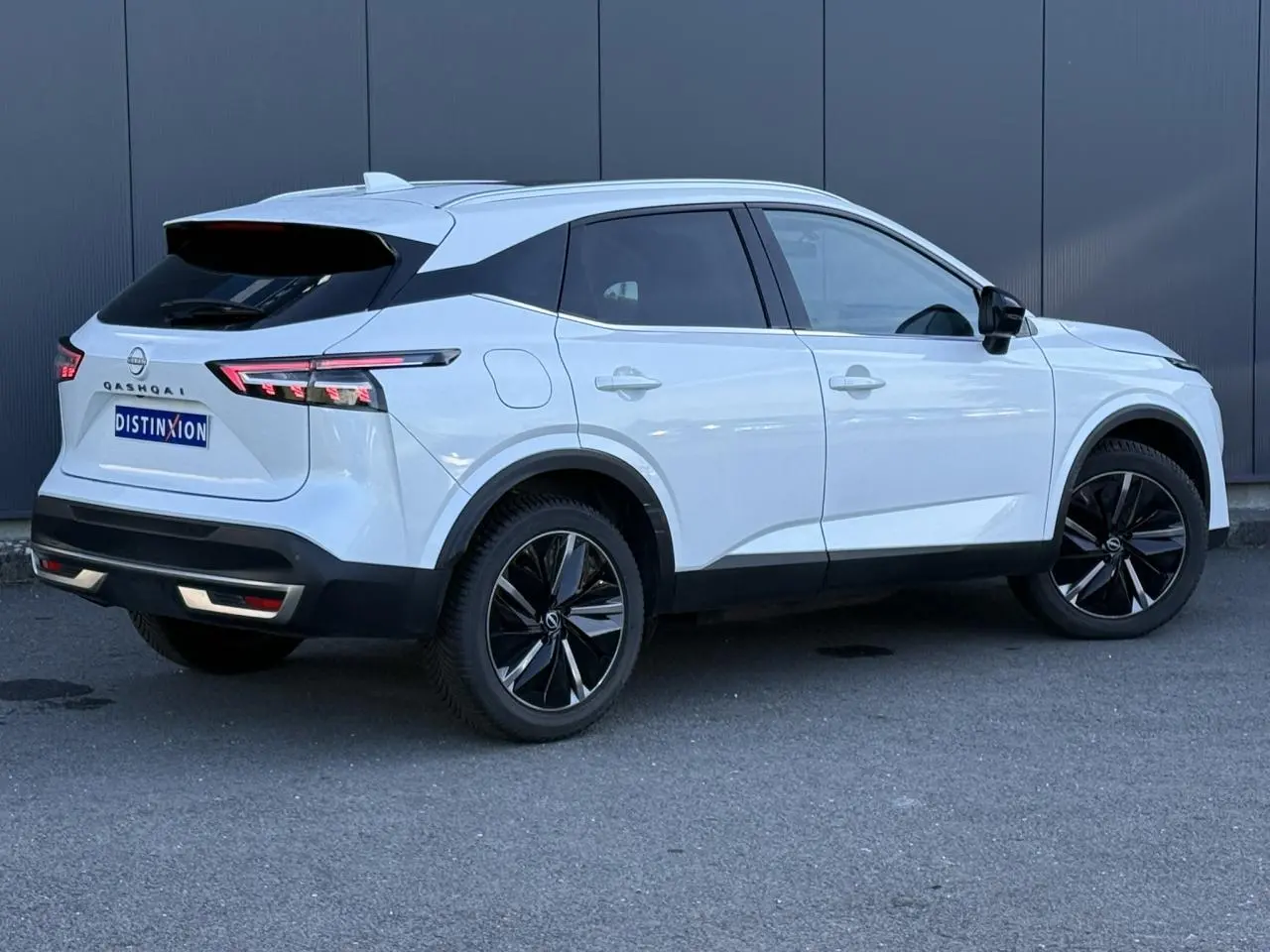 Nissan Qashqai blanc nacré en 3/4 arrière droit, avec jantes alliage noires et feux arrière LED distinctifs.