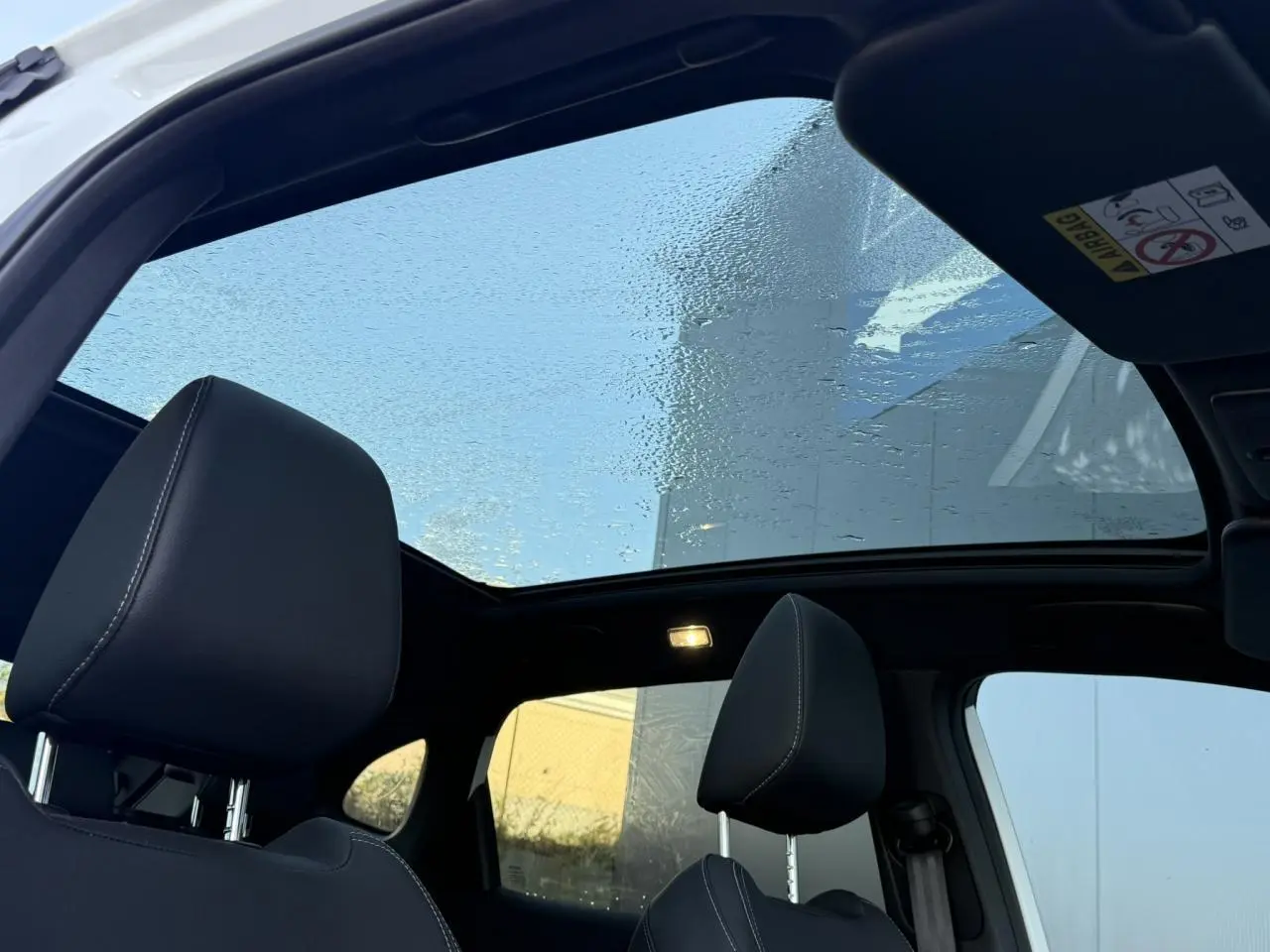 Vue intérieure du toit panoramique en verre du Nissan Qashqai blanc nacré avec sièges avant noirs et ciel de toit noir.