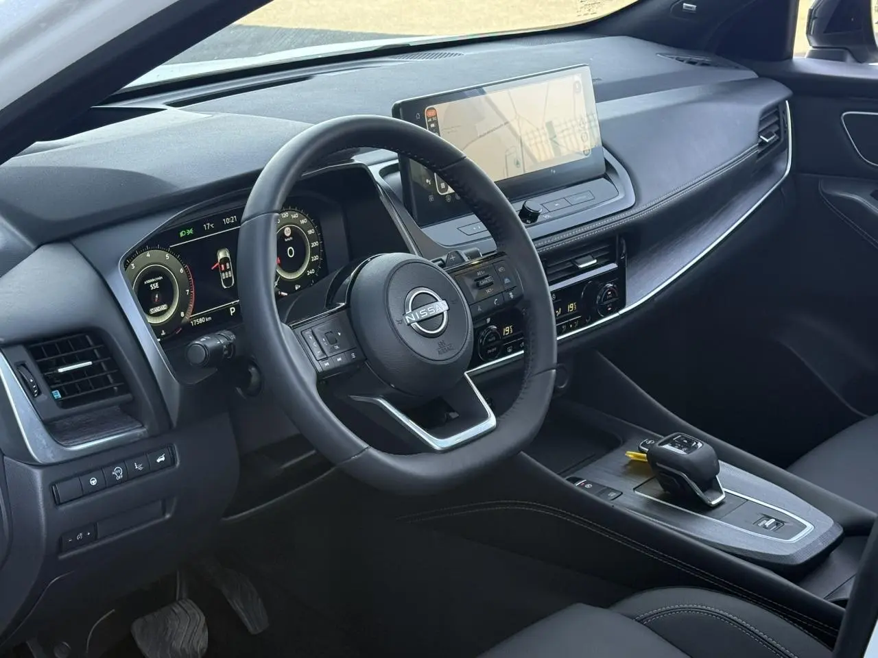 Vue intérieure côté conducteur du tableau de bord noir du Nissan Qashqai 2025 avec écran tactile et volant cuir.