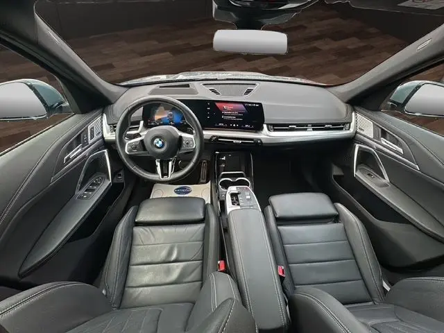 Vue intérieure avant du BMW X1 Storm Bay 2024, sellerie cuir Vernasca noire, tableau de bord moderne avec écran tactile large.
