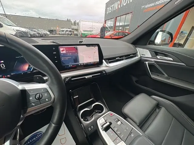 Intérieur BMW X1 XDRIVE 23D 2024, vue côté conducteur, sellerie cuir noire Vernasca et écran tactile central.