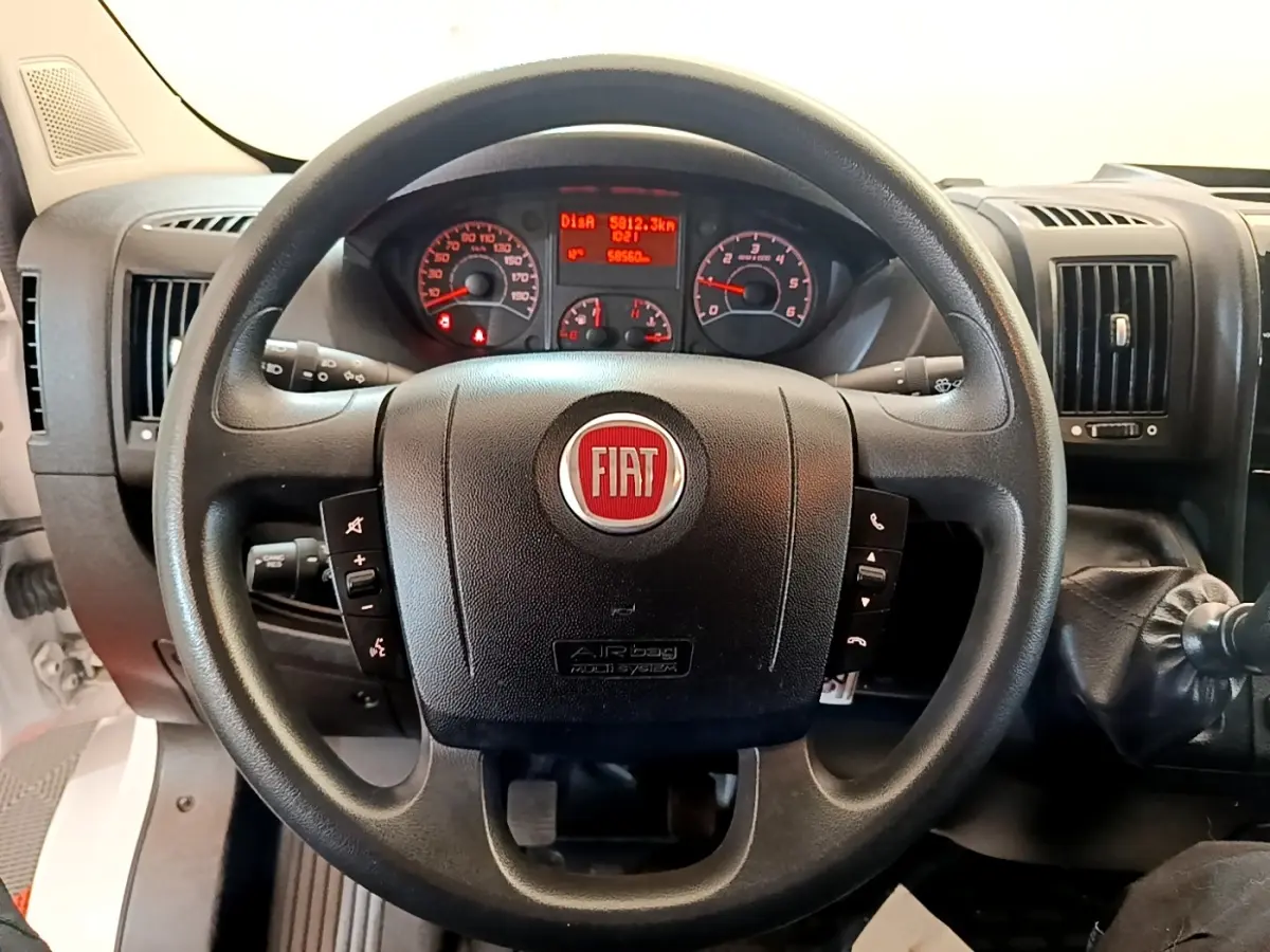 Vue rapprochée du volant noir multifonctions avec logo FIAT rouge et tableau de bord éclairé du Fiat Ducato Fourgon blanc.